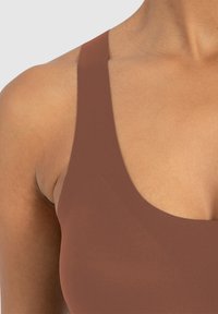 Bruine sportbeha met brede banden, een gladde textuur en een lage ronde halslijn, ontworpen voor comfort en ondersteuning.