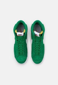 Höga gröna mockaskor med vita detaljer, snörningsdesign och vadderad krage med svarta och gula inslag på insidan.