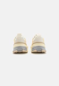 Zapatillas deportivas de color claro con un upper de malla y material sintético, cuello acolchado y una suela gruesa y acolchada con acentos grises y beige.