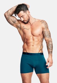 Turkosa boxershorts med svart elastisk midja som har "BODYFRANK"-logga. Slät tyg, figursydd design, midjehöjd längd.