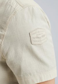 Beige Kurzarmhemd aus strukturiertem Stoff. Enthält ein gesticktes Badge auf der Schulter mit dem Text "PME Legend Aviator."