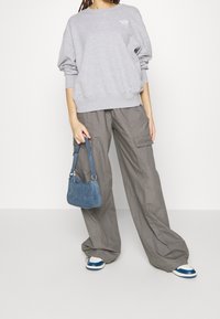 Šedá mikina s logem, široké šedé cargo kalhoty s kapsami, modrá džínová taška a modro-bílé tenisky. Bez výrazných vzorů.