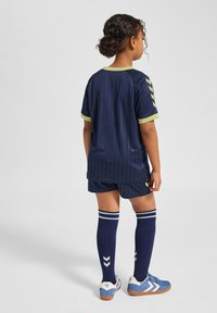 Marinblå idrottsuniform med horisontella ränder, kontrasterande grön krage och matchande shorts. Blå och vita skor med randiga blå strumpor.