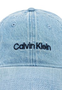 Cappellino da baseball in denim azzurro chiaro con logo ricamato "Calvin Klein" in blu navy. Texture liscia con visiera curva e dettagli di cucitura.
