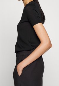 Top corto nero a maniche corte realizzato in tessuto leggero, con scollatura rotonda e una vestibilità comoda, abbinato a pantaloni scuri con vita elastica.