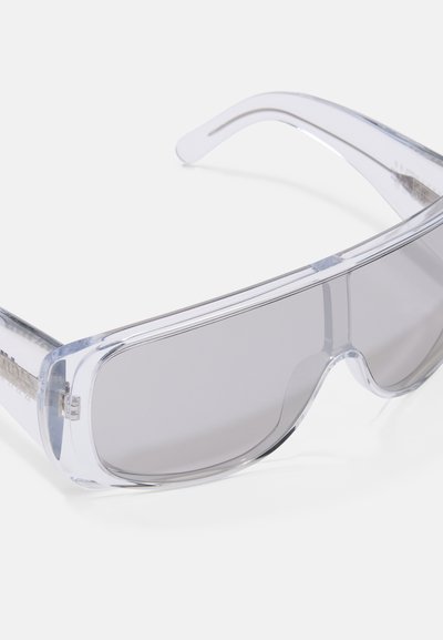 Óculos de proteção transparentes com lentes largas e retangulares, com tonalidade, e uma armação transparente, inclinados contra um fundo branco.