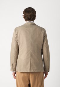 Beige blazer van een gestructureerde stof, met een enkele rugventilatie en twee knopen bij de manchetten. Heeft een slim fit en gestructureerde schouders.