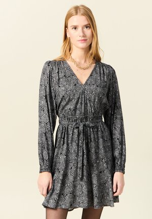 Vestido negro de manga larga con estampado floral, escote en V, cintura elástica y cinturón de lazo, terminado con un dobladillo acampanado.