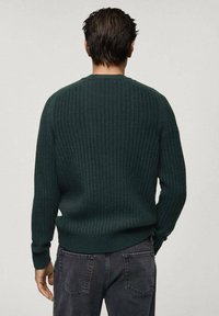 Maglione ribbed verde scuro con maniche lunghe, collo rotondo e un motivo a maglia testurizzato, abbinato a pantaloni grigio scuro.
