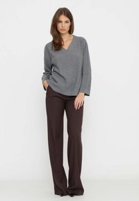 Maglione grigio a scollo a V con vestibilità ampia, abbinato a pantaloni marroni a vita alta e gamba larga. Texture lisce, design minimalista.