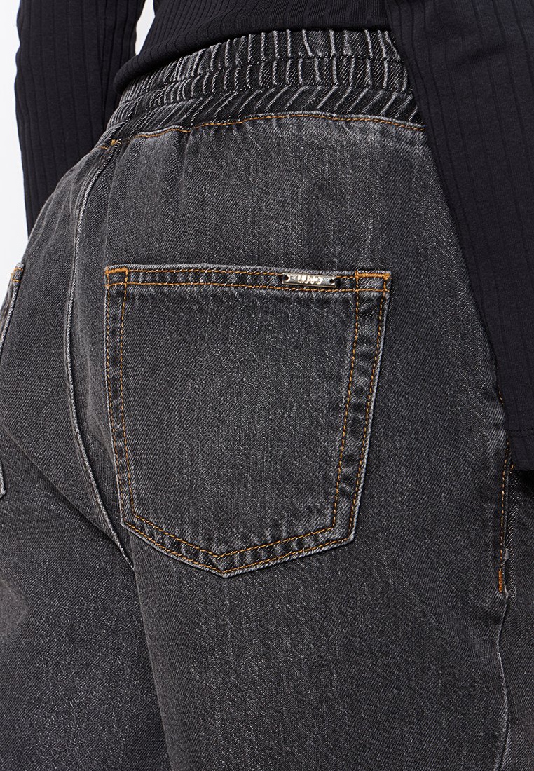 I pantaloni in denim nero presentano una vita alta con elastico, una tasca posteriore con cuciture arancioni e una texture liscia e opaca.