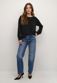 Juodas ilgomis rankovėmis viršus, derinamas su šviesiai mėlynomis aukštu liemeniu džinsais ir juodais stiletto aukštakulniais. Viršus turi apvalų kaklą ir laisvą kirpimą.