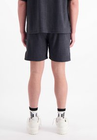 Zwarte tshirt met korte mouwen en bijpassende shorts met een gestructureerd ruitpatroon. Gecombineerd met witte sneakers en gestreepte zwart-witte sokken.