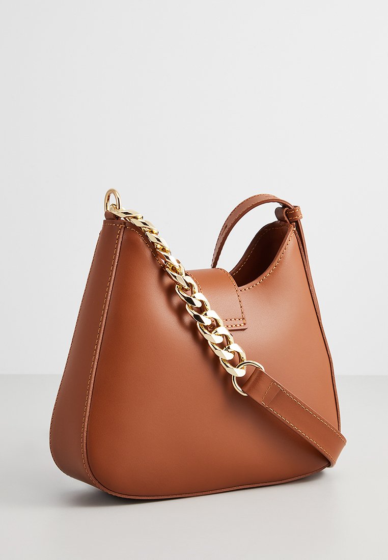 Sac à main en cuir marron avec une forme structurée, accentué par une bandoulière en chaîne dorée et une courte poignée. Texture lisse avec des détails de couture minimaux.