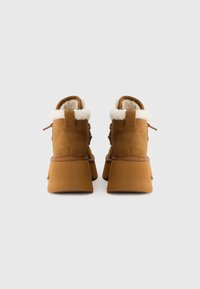 Bottines en suede marron avec un col en fausse fourrure blanche, semelle épaisse et détails en dentelle à l'arrière. Fini texturé visible.