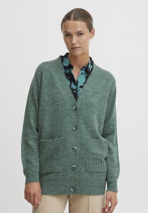 Cardigan en tricot vert avec un col en V, poches côtelées et cinq boutons. Présente une finition texturée avec une coupe décontractée et des manches longues.