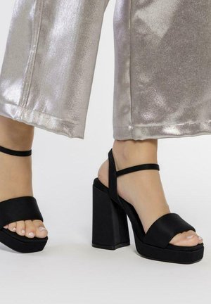 Sandales plates noires avec un talon épais, dotées de larges brides avant et d'une fine bride de cheville. Fini texturé et lisse.