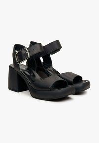 Zwarte leren sandaal met hakken, met een open teen, enkelschoenen met een zilveren gesp en een robuuste blokhak. Glad oppervlak en minimalistisch design.