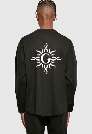 Schwarzes Langarmshirt mit einem großen weißen Sonnendesign, das geschwungene Strahlen und einen runden Mittelpunkt aufweist. Hergestellt aus weichem Baumwollstoff.