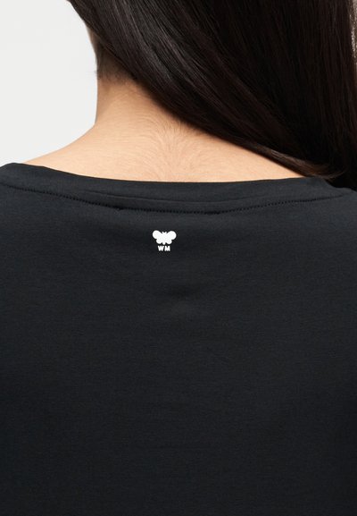 Μαύρο πουκάμισο με στρογγυλή λαιμόκοψη και ένα μικρό λευκό γραφικό πεταλούδας με τα γράμματα «WM» κάτω από αυτήν στο πίσω μέρος του γιακά.
