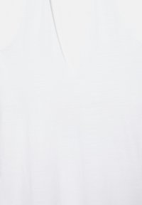 Gros plan d'un tissu blanc avec un détail subtil de couture en forme de V, montrant une texture lisse et de légers plis.