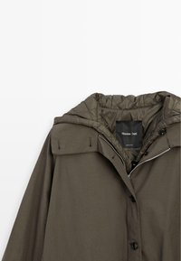 Veste à capuche vert olive avec doublure matelassée, fermeture à boutons et zip, et une étiquette noire "Massimo Dutti" à l'intérieur du col.