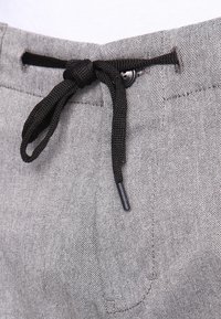 Shorts en tissu gris avec une texture tissée, dotés d'un cordon de serrage noir et d'un bouton à la taille pour un ajustement.