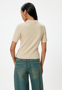 Beige geribbelde gebreide polo met korte mouwen, gecombineerd met hoog-waist blauwe denim jeans met achterzakken en een relaxte pasvorm.
