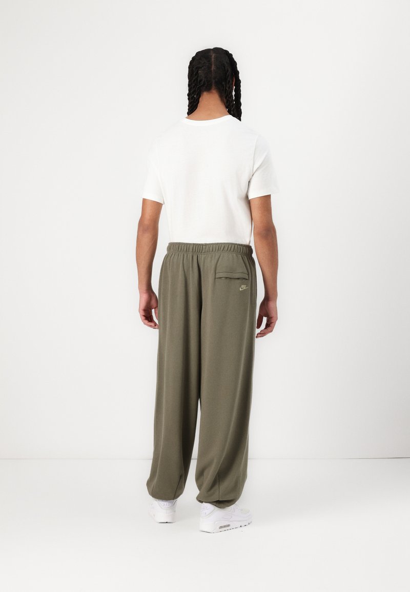 Oliwkowe, luźne spodnie z elastycznym pasem i tylną kieszenią; w komplecie z białą koszulką z krótkim rękawem i białymi trampkami.