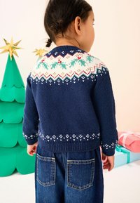 Granatowy sweter z dzianiny z wzorzystymi detalami w bieli, czerwieni i zieleni na karczku. Połączony z niebieskimi dżinsami z tylnymi kieszeniami.