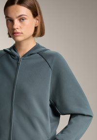 Giacca con cappuccio e zip in tessuto blu scuro testurizzato, caratterizzata da un design a coste, maniche raglan e una vestibilità comoda.