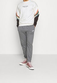 Felpa bianca con strisce multicolori e logo, abbinata a pantaloni jogger grigi con un piccolo logo Nike e sneakers rosse a collo alto.