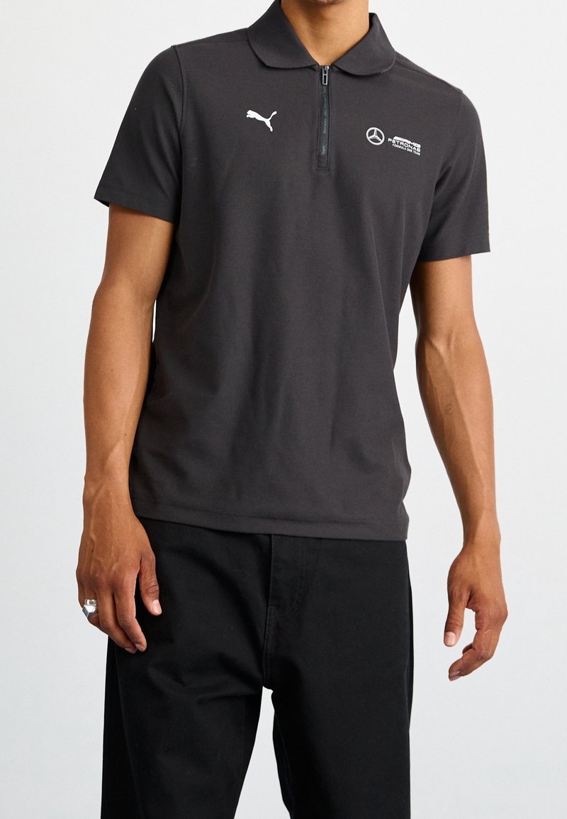 Polo noir en mélange de coton, avec une fermeture éclair sur le devant, des manches courtes et des logos blancs de Puma et Mercedes-Benz sur la poitrine.