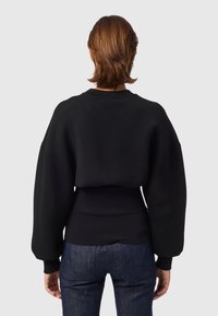 Černá oversize mikina s texturovaným žebrovaným lemem, balónovými rukávy a kulatým výstřihem, kombinovaná s tmavými džínami.