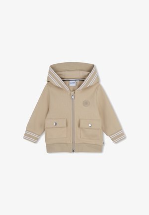 Sweat à capuche beige zippé avec une capuche, deux poches avant et des accents rayés blancs sur la capuche. Présente un logo sur la poitrine. Texture de tissu doux.