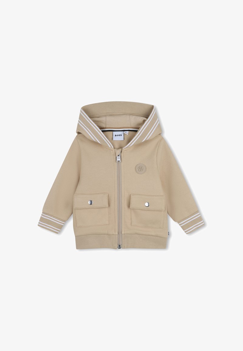 Felpa con cappuccio beige con zip, due tasche frontali e dettagli a strisce bianche sul cappuccio. Presenta un logo sul petto. Tessuto dalla texture morbida.