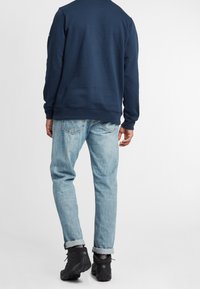 Felpa blu navy, jeans azzurri con risvoltini, e scarpe da esterno nere. Design semplice con vestibilità comoda, in materiale di cotone.