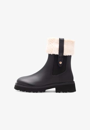 Schwarze Leder Stiefeletten mit einem weißen Kunstfellumschlag, elastischen Seitenpaneelen und einer stabilen schwarzen Gummisohle mit strukturiertem Profil.