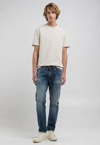 Ljust beige bomull t-shirt med korta ärmar, kombinerad med blå denimjeans med en urtvättad textur, och vita sneakers.