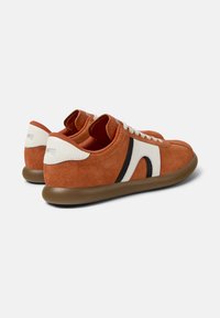 Braune Wildledersneaker mit weißen und schwarzen Designelementen, runder Zehenpartie, Schnürung und einer flexiblen Gummisohle.