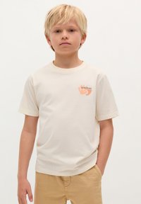 Cremfarbendes T-Shirt mit kurzen Ärmeln aus Baumwolle, das ein Handgrafik und den Text "SCALPERS" in Orange und Grau auf der linken Brust zeigt.