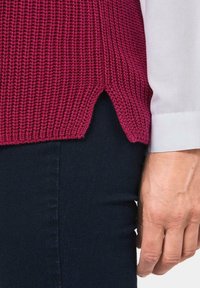 Bordeaux gebreide top met zijsplitten, textuurstof en een losse pasvorm. Gepaard met donkere denim, met een frisse witte mouwdetail.