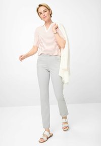 Gestreepte polo met korte mouwen in koraal en wit, gecombineerd met lichtgrijze slim-fit broek en beige sandalen. Een witte gebreide trui over een arm gedrapeerd.