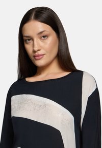 Zwarte blouse met een brede halslijn, voorzien van witte abstracte patronen en glinsterende accenten. Zachte stof met een ontspannen pasvorm en lange mouwen.