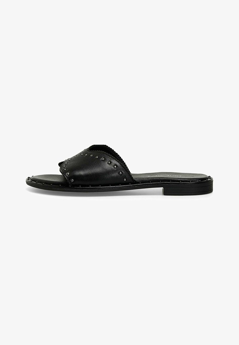 Black leather slide sandal featuring a wide strap with stud detailing, smooth texture, and flat sole for comfort.