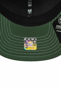 Grüner Hut mit einem schwarzen Schild, verziert mit weißen Nähten. Enthält einen NFL-Hologramm-Aufkleber auf der Innenseite des Schirms.