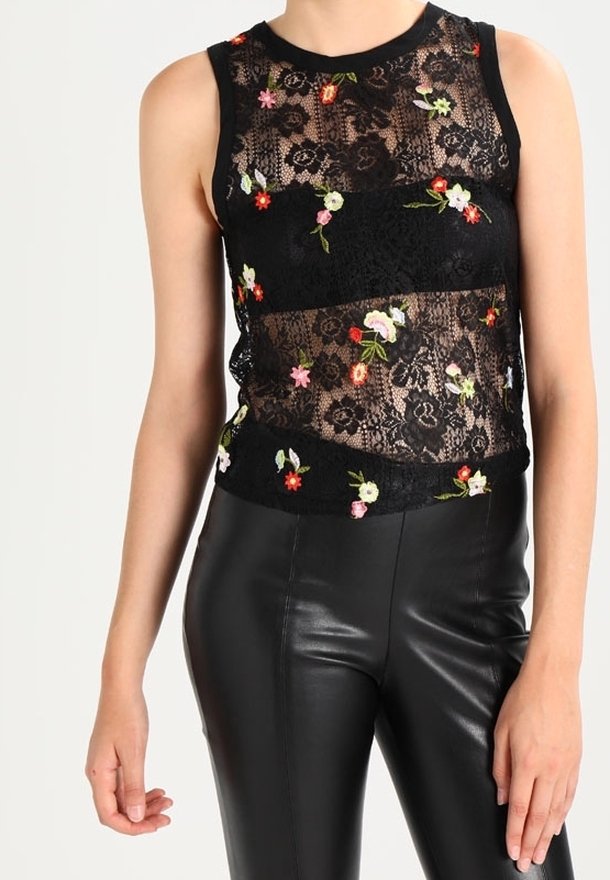 Haut sans manches en dentelle noire avec broderie florale colorée associé à un pantalon en cuir noir taille haute sur une personne debout.