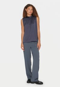 Top senza maniche di un blu navy scuro con scollatura plissettata, abbinato a pantaloni larghi grigi chiari e scarpe nere chunky. Tessuto morbido e vestibilità rilassata.
