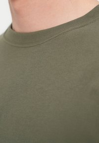 Λαδί βαμβακερό t-shirt με στρογγυλή λαιμόκοψη, με ομαλή υφή και διπλή ραφή κατά μήκος του γιακά για ανθεκτικότητα.