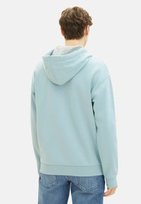 Sudadera con capucha de color azul claro, con un corte relajado, tejido texturizado y un forro gris en la capucha. Combinada con unos clásicos vaqueros azules.